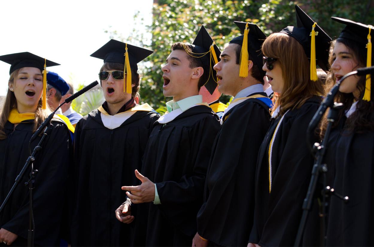罗彻斯特大学的毕业生戴着帽子，穿着长袍，在毕业典礼上唱着母校的歌